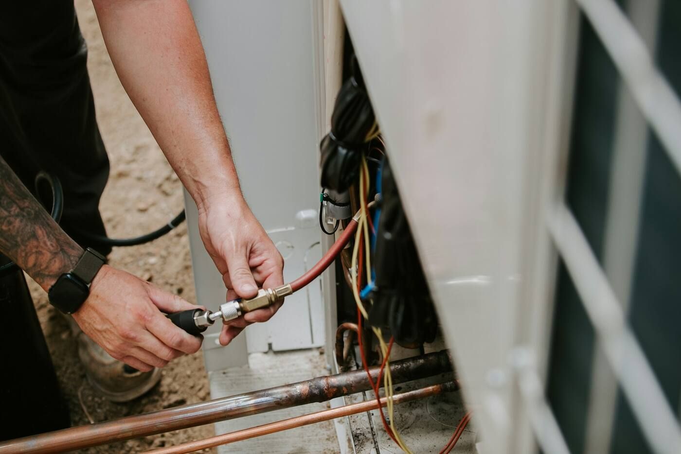 A technician's hands connecting a gauge hose to the service valve of an outdoor AC unit