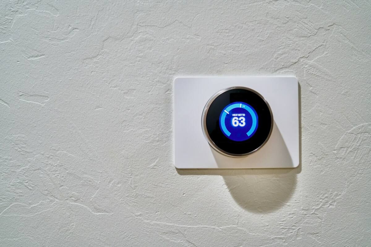 A round thermostat on a textured wall, set to heat to 63 degrees